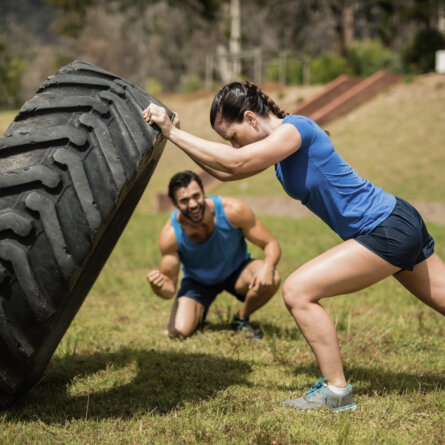 Fit woman flipping a tire while trainer cheering