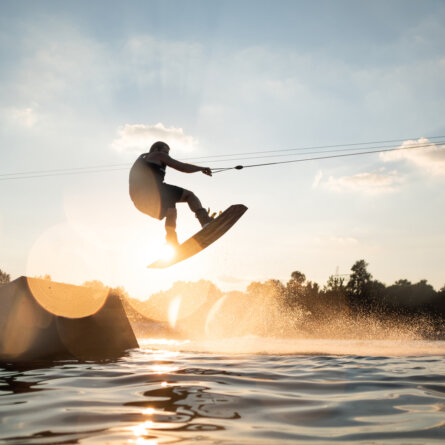 Stock photo of a young man wakeboarding on the lake, jumping off the ramp