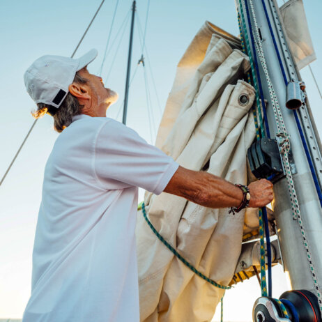 Mature captain looking up while adjusting sail. Senior yachtsman